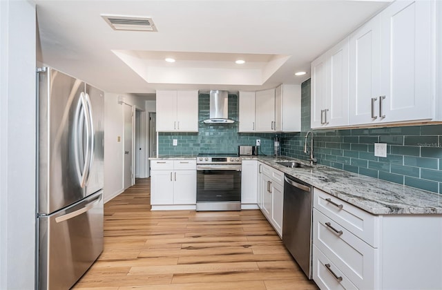 kitchen featuring white cabinets, stainless steel appliances, a tray ceiling, and wall chimney exhaust hood