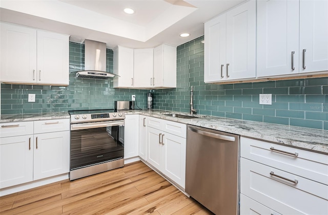 kitchen featuring light wood-type flooring, stainless steel appliances, white cabinetry, and wall chimney range hood