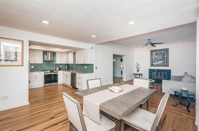 dining room featuring ceiling fan, sink, a textured ceiling, and light hardwood / wood-style flooring