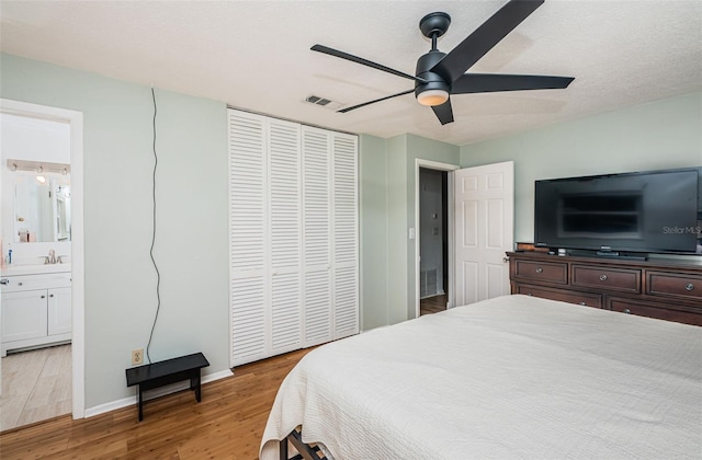 bedroom featuring ensuite bathroom, light hardwood / wood-style flooring, ceiling fan, a textured ceiling, and a closet