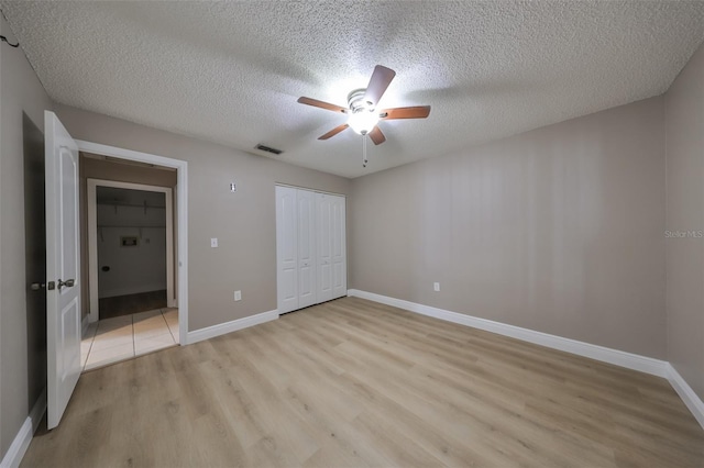 unfurnished bedroom featuring ceiling fan, a closet, a textured ceiling, and light wood-type flooring