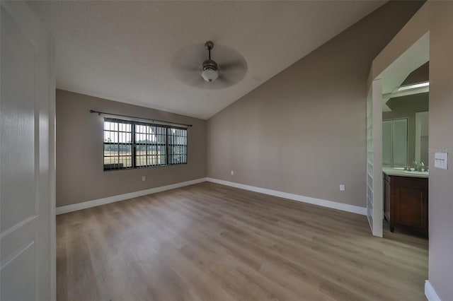 spare room with a textured ceiling, vaulted ceiling, ceiling fan, sink, and light hardwood / wood-style flooring