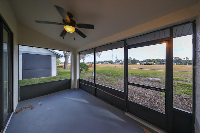 unfurnished sunroom featuring a wealth of natural light, ceiling fan, a rural view, and lofted ceiling