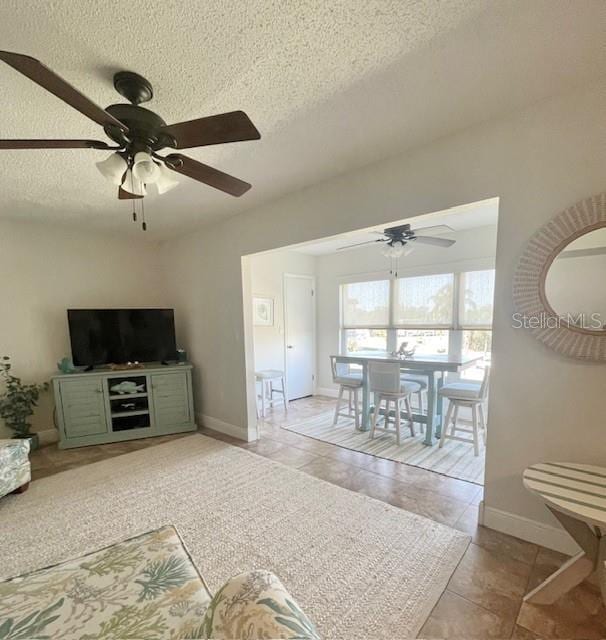 living room with ceiling fan, light tile patterned floors, and a textured ceiling