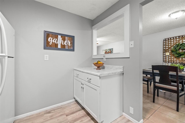 kitchen featuring white refrigerator, white cabinetry, a textured ceiling, and light hardwood / wood-style flooring