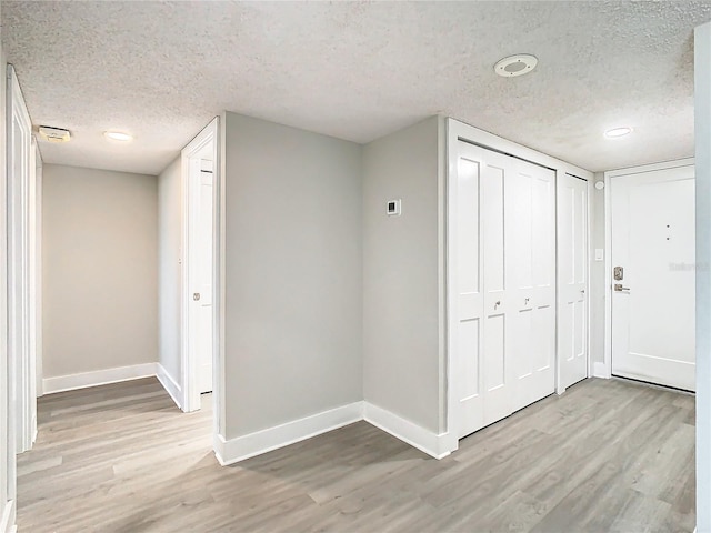 corridor with a textured ceiling and light hardwood / wood-style flooring