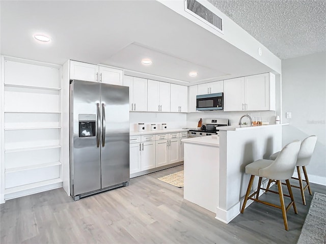 kitchen with appliances with stainless steel finishes, a textured ceiling, white cabinets, light hardwood / wood-style floors, and a breakfast bar area