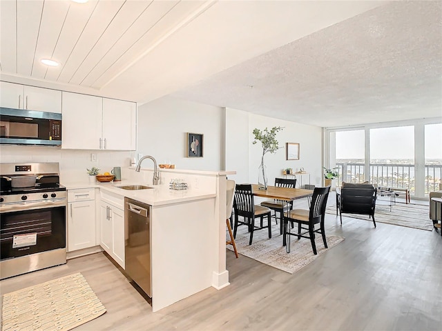 400 Island Way Unit 1411, Clearwater Beach, FL 33767 - kitchen with stainless steel appliances, a sink, light wood-style flooring, a peninsula, and white cabinets