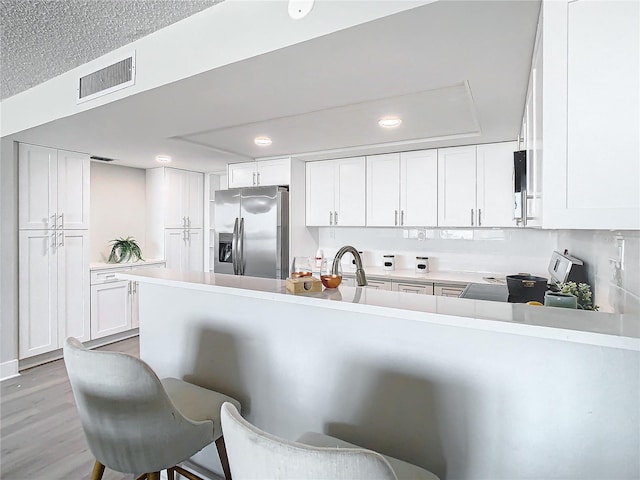 kitchen with a kitchen breakfast bar, stainless steel fridge with ice dispenser, kitchen peninsula, white cabinets, and light wood-type flooring