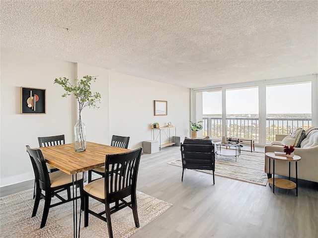 dining area with expansive windows, light hardwood / wood-style flooring, a water view, and a textured ceiling