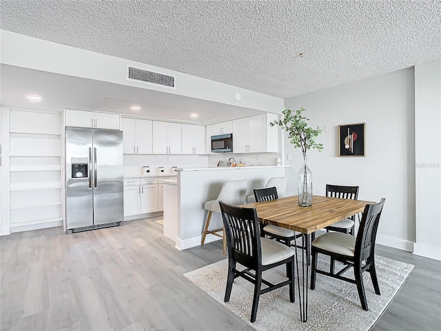 dining space with a textured ceiling and light hardwood / wood-style flooring