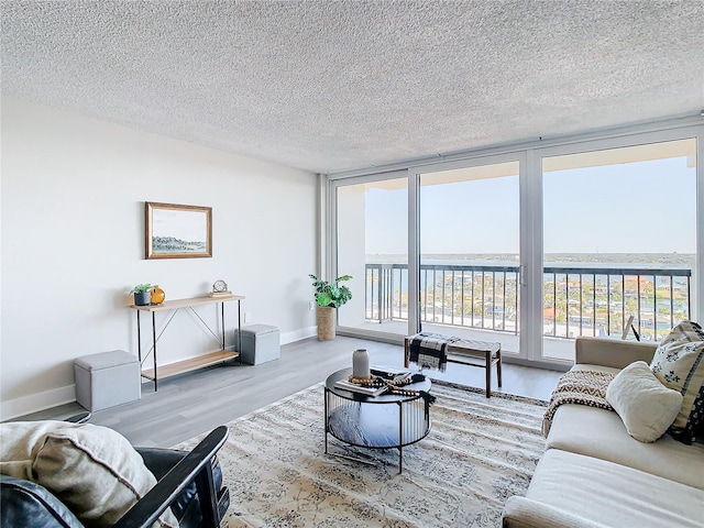 living room with expansive windows, hardwood / wood-style floors, a water view, and a textured ceiling