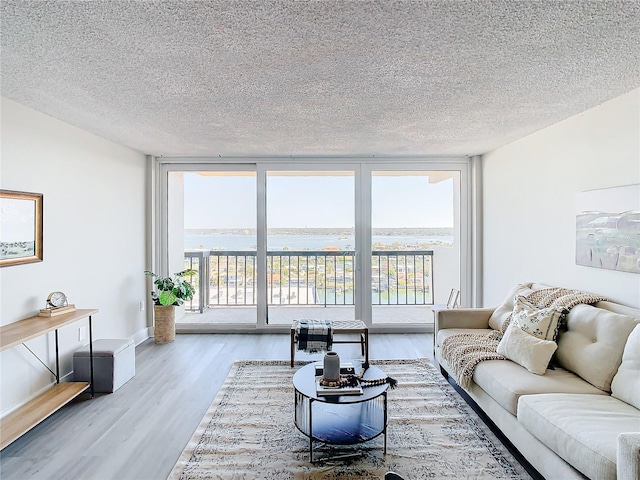 living room with wood-type flooring, a textured ceiling, a water view, and a wall of windows