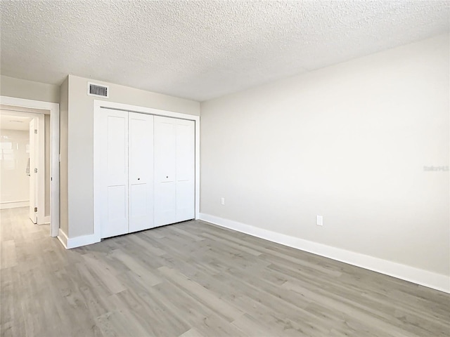 unfurnished bedroom featuring light wood-type flooring, a textured ceiling, and a closet