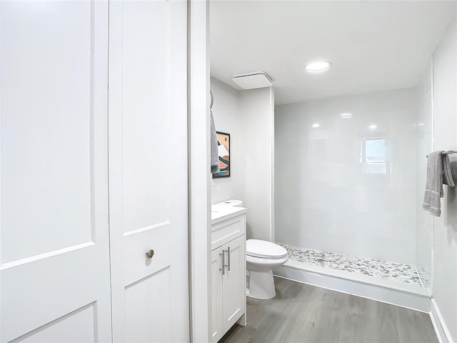 bathroom with tiled shower, vanity, wood-type flooring, and toilet