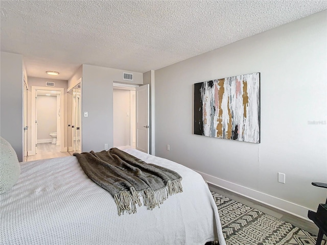 bedroom featuring connected bathroom, a closet, hardwood / wood-style floors, and a textured ceiling