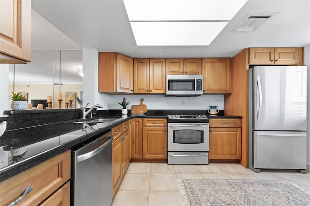 kitchen featuring light tile patterned flooring, stainless steel appliances, dark stone counters, and sink