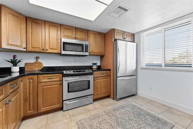 kitchen featuring appliances with stainless steel finishes, light tile patterned floors, and dark stone counters