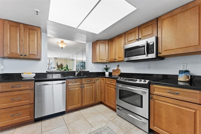 kitchen featuring light tile patterned flooring, appliances with stainless steel finishes, dark stone counters, and sink