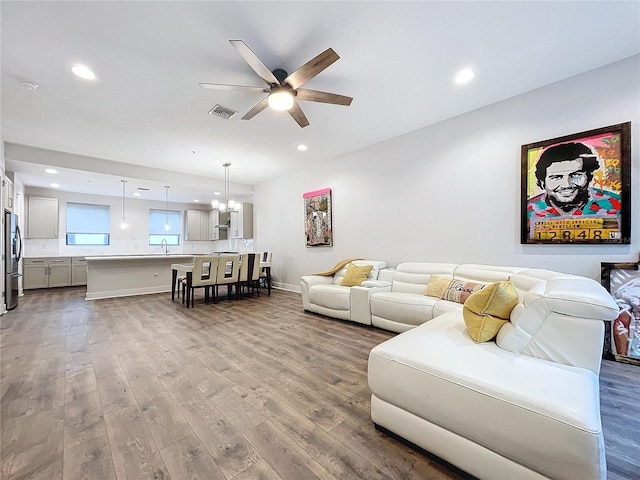 living room with sink, ceiling fan with notable chandelier, and light wood-type flooring