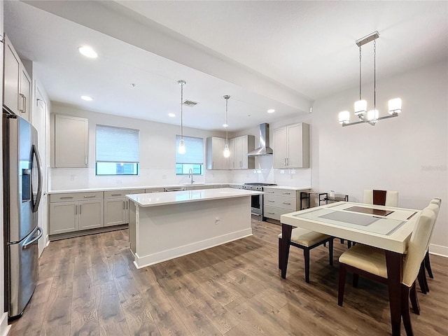 kitchen with a center island, wall chimney exhaust hood, hanging light fixtures, dark hardwood / wood-style flooring, and appliances with stainless steel finishes