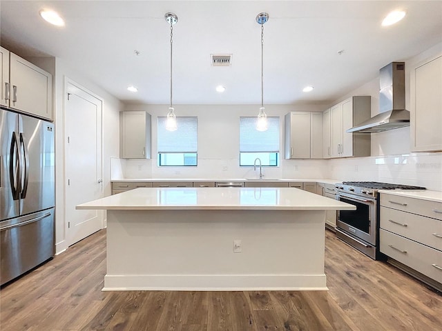 kitchen with appliances with stainless steel finishes, wall chimney exhaust hood, sink, hardwood / wood-style flooring, and a center island