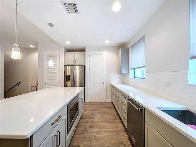 kitchen with hanging light fixtures, tasteful backsplash, appliances with stainless steel finishes, a kitchen island, and hardwood / wood-style flooring