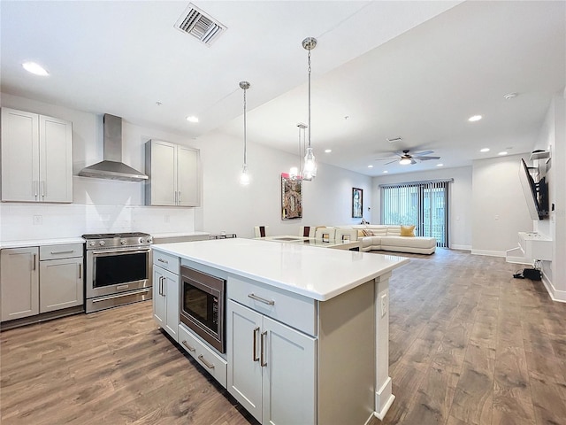 kitchen featuring gray cabinetry, wall chimney range hood, ceiling fan, wood-type flooring, and stainless steel appliances