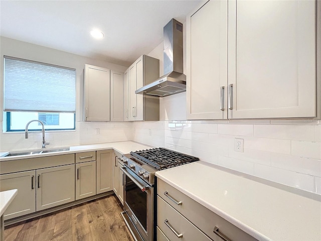 kitchen featuring high end range, light wood-type flooring, tasteful backsplash, wall chimney exhaust hood, and sink