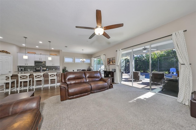 carpeted living room featuring ceiling fan with notable chandelier and plenty of natural light