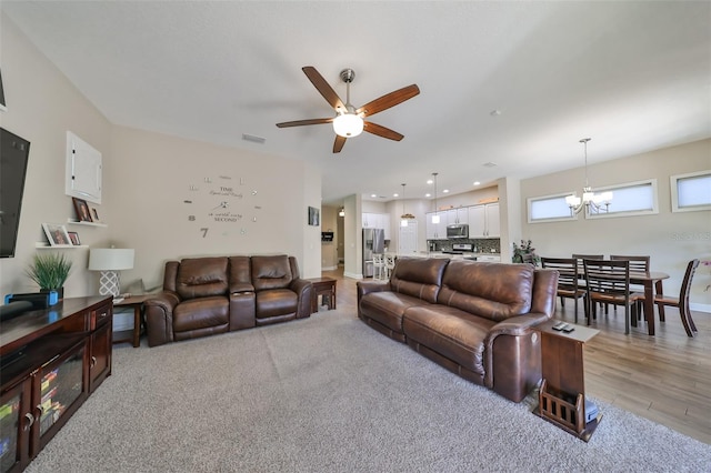 living room with ceiling fan with notable chandelier and light wood-type flooring