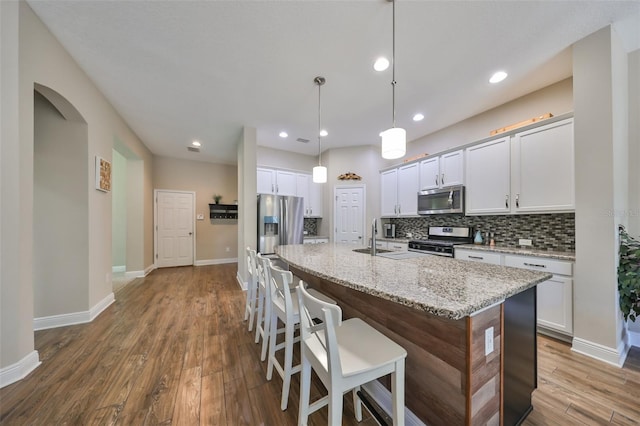 kitchen with light stone countertops, appliances with stainless steel finishes, a kitchen island with sink, hardwood / wood-style floors, and white cabinetry