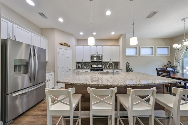 kitchen with pendant lighting, a kitchen island with sink, sink, white cabinetry, and stainless steel appliances