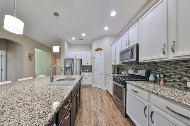 kitchen featuring white cabinets, pendant lighting, stainless steel appliances, and light hardwood / wood-style floors