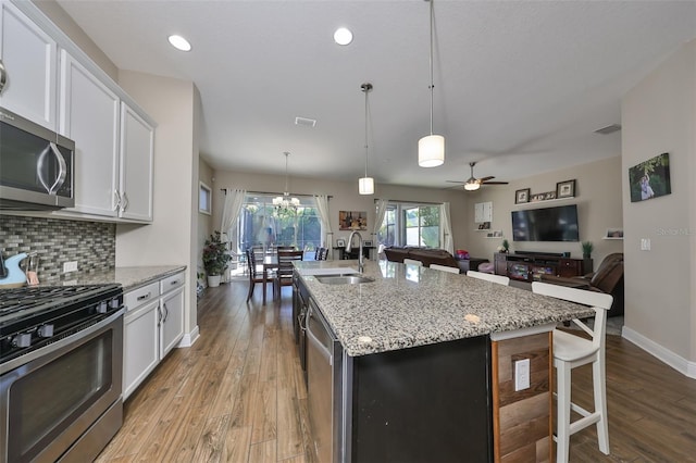 kitchen with a kitchen island with sink, hanging light fixtures, sink, appliances with stainless steel finishes, and white cabinetry