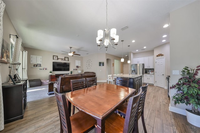 dining space featuring ceiling fan with notable chandelier, light hardwood / wood-style floors, and sink