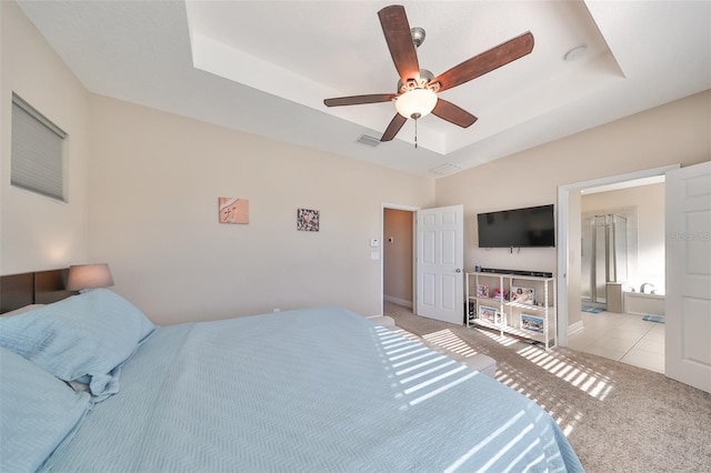 bedroom with ensuite bathroom, a raised ceiling, ceiling fan, and light colored carpet