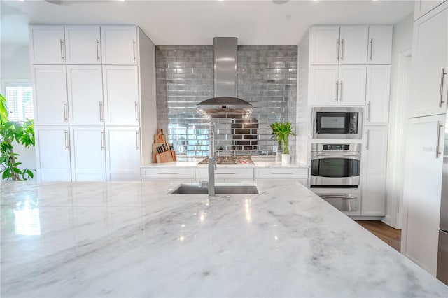 kitchen with wall chimney range hood, black microwave, light stone countertops, white cabinets, and oven