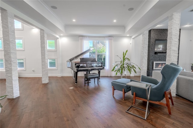 sitting room featuring hardwood / wood-style flooring, ornamental molding, a stone fireplace, a raised ceiling, and ornate columns