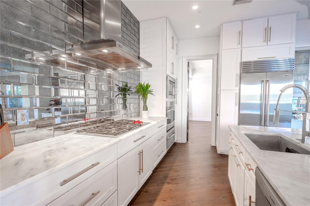 kitchen featuring tasteful backsplash, white cabinetry, sink, island exhaust hood, and light stone countertops