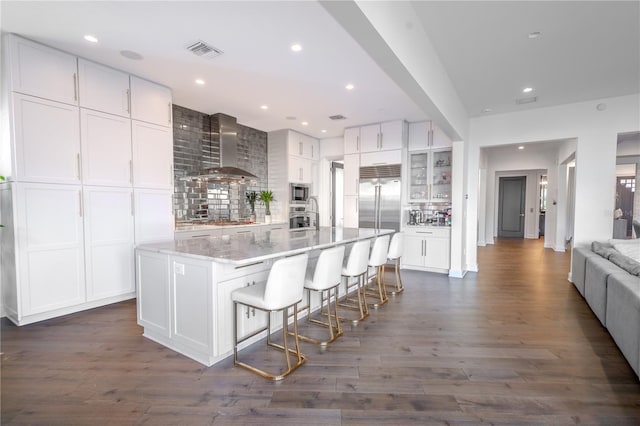 kitchen featuring a breakfast bar, dark hardwood / wood-style floors, white cabinets, a center island with sink, and wall chimney exhaust hood