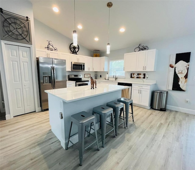 kitchen with lofted ceiling, white cabinets, light hardwood / wood-style floors, appliances with stainless steel finishes, and a kitchen island