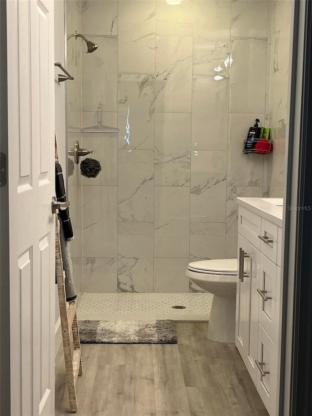 bathroom with tiled shower, toilet, vanity, and hardwood / wood-style flooring