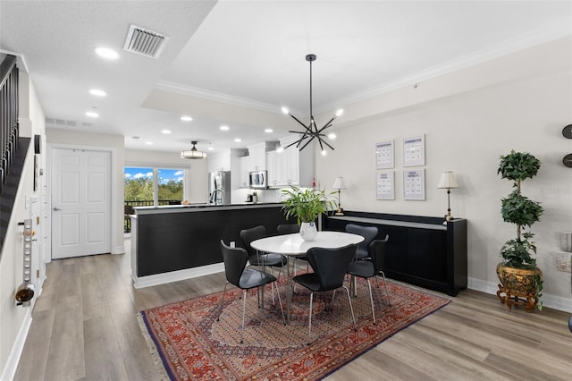 dining room with light hardwood / wood-style flooring, crown molding, and a notable chandelier