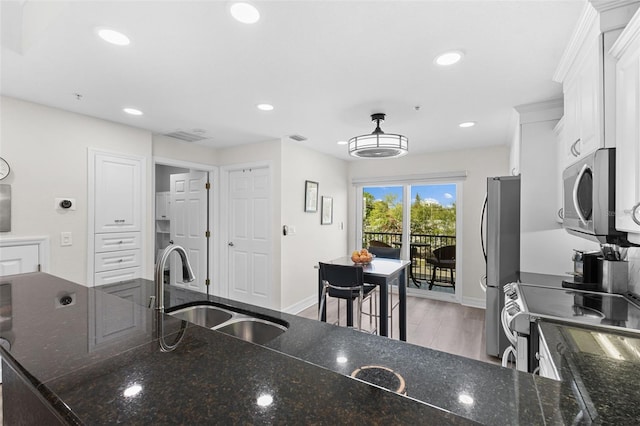 kitchen featuring white cabinetry, sink, dark stone counters, appliances with stainless steel finishes, and light wood-type flooring