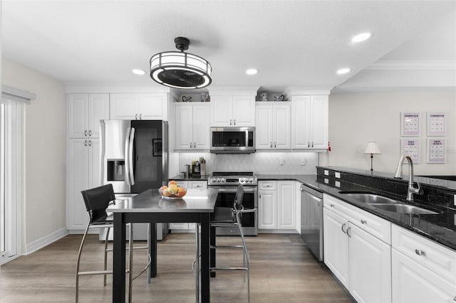 kitchen featuring appliances with stainless steel finishes, a sink, backsplash, white cabinetry, and light wood finished floors