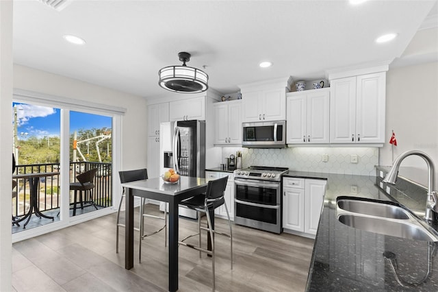 kitchen featuring appliances with stainless steel finishes, a sink, tasteful backsplash, light wood-style flooring, and recessed lighting