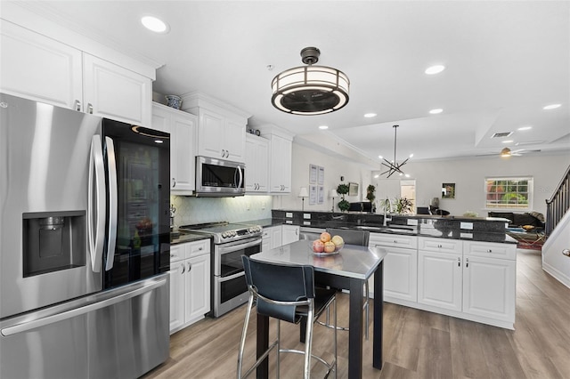 kitchen with stainless steel appliances, a peninsula, recessed lighting, a sink, and white cabinetry