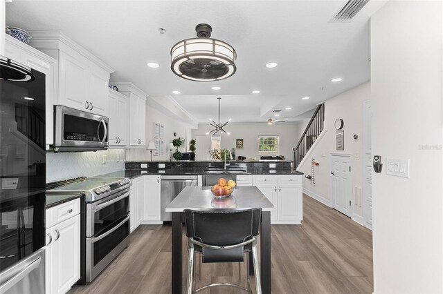 kitchen featuring appliances with stainless steel finishes, a sink, a peninsula, wood finished floors, and white cabinetry