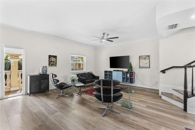 living area with stairway, ceiling fan, wood finished floors, ornamental molding, and baseboards